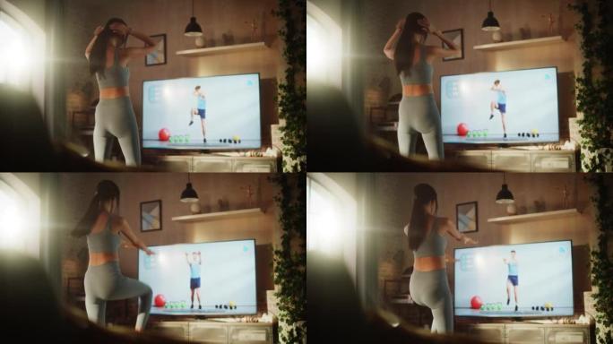家庭健身房: 通过在线视频应用程序与私人教练一起训练的漂亮女孩。在健身流媒体应用程序中使用电视锻炼服