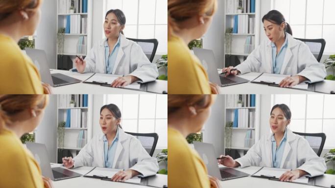 年轻的亚洲女性医生在白色医疗制服使用笔记本电脑正在传递伟大的新闻谈话讨论结果或症状与女孩患者坐在办公