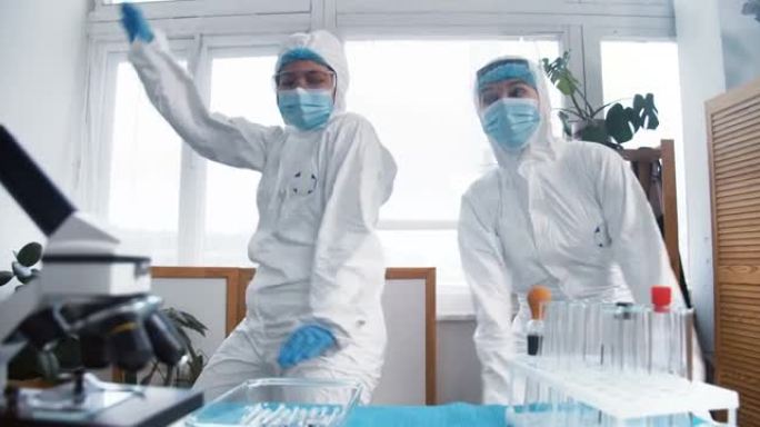 抗击病毒大流行的结束。两个穿着化学防护服的快乐有趣的女医生做疯狂的庆祝舞蹈。