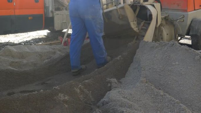特写: 男工人将一勺黑色熨平板沙子推向机器。