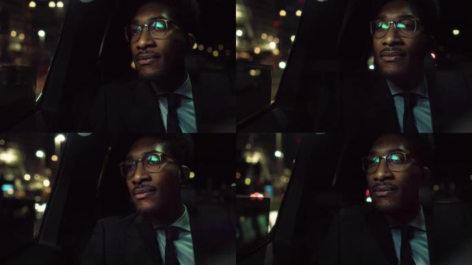 穿着眼镜的时髦黑人的肖像晚上正坐在出租车的后座上通勤回家。商业首席执行官看着窗外，在温暖的灯光下，在