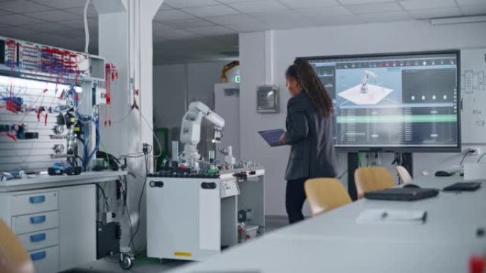 在工厂: 自动化黑色工程师使用笔记本电脑对机械臂进行编程，同时坐在桌子上，然后去机器人。自动制造业概