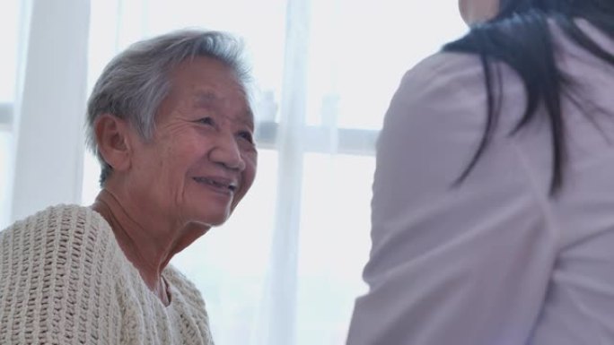 亚洲年轻女护士医生牵着亚洲高级祖母病人的手帮助表达同理心鼓励在家就诊时告诉诊断。在家护理人员