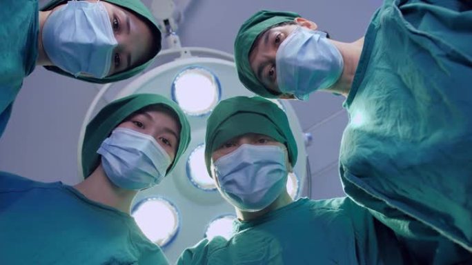 由四名外科医生组成的团队穿着防护服准备手术，在手术灯的背景下俯视摄像机。观点概念