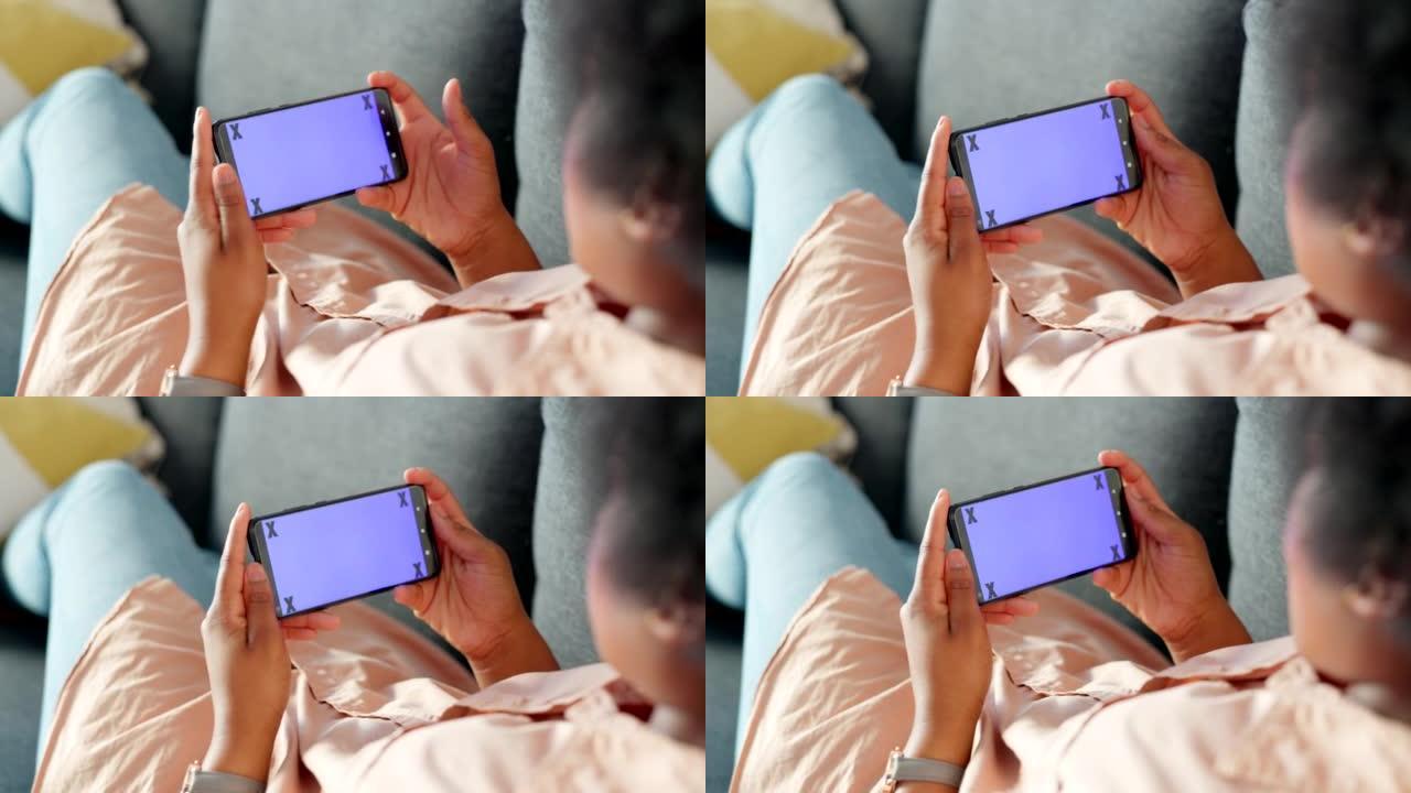 舒适的女士看互联网视频。玩家拿着空白的手持手机屏幕放松，坐在家里的沙发上。在风景模式下玩游戏的人在房