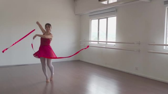 慢动作亚洲中国少女在体操学校用彩带练习艺术体操。芭蕾舞学校。