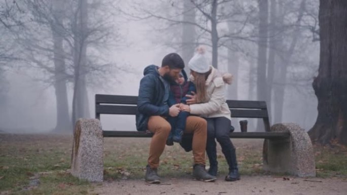 父母与儿子坐在公园里满是雾的长凳上