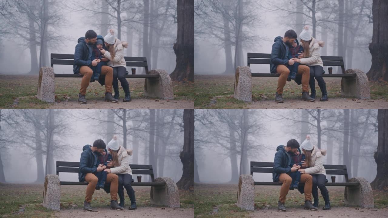 父母与儿子坐在公园里满是雾的长凳上
