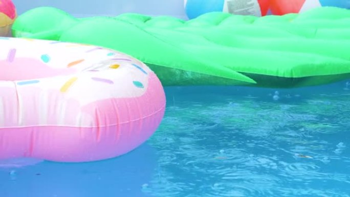 特写: 雨滴落在空水池周围漂浮的彩色玩具上。