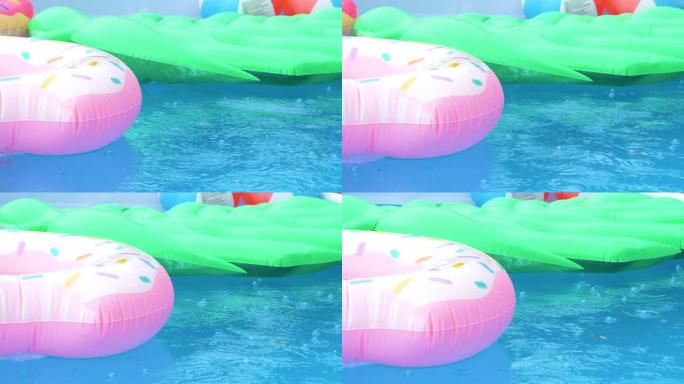 特写: 雨滴落在空水池周围漂浮的彩色玩具上。