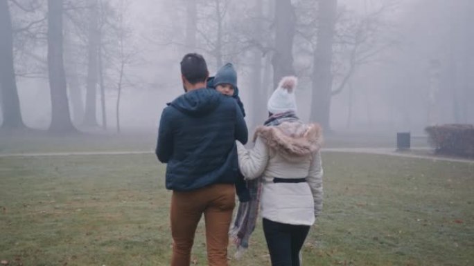 父亲带着儿子与母亲一起在雾蒙蒙的公园散步