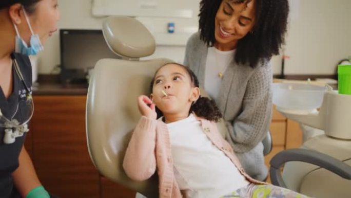 在牙医检查和牙齿矫正医生预约后，小女孩吮吸棒棒糖。可爱的女性孩子在完成口腔或牙科检查后吃了甜蜜的奖励