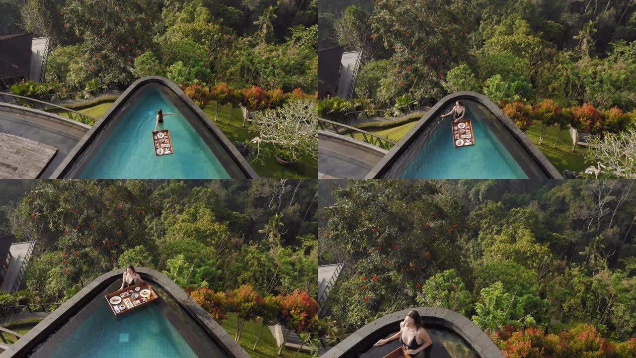 鸟瞰图女人在游泳池吃早餐，在豪华酒店水疗中心享受异国美食，可以看到热带丛林