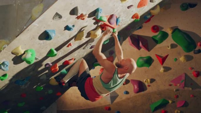 经验丰富的攀岩者在健身房的抱石墙上练习单人攀岩。男子在室内健身设施锻炼，进行极限运动以进行健康训练。