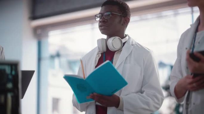 一名年轻的黑人男工科学生在实验室提问和做笔记的肖像。实验室助理在一次会议上展示了主动性和想法，与他的