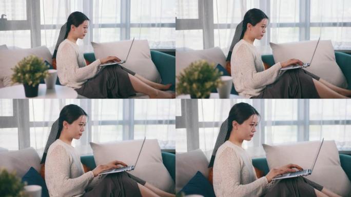 年轻女性在家中使用笔记本电脑坐在沙发上