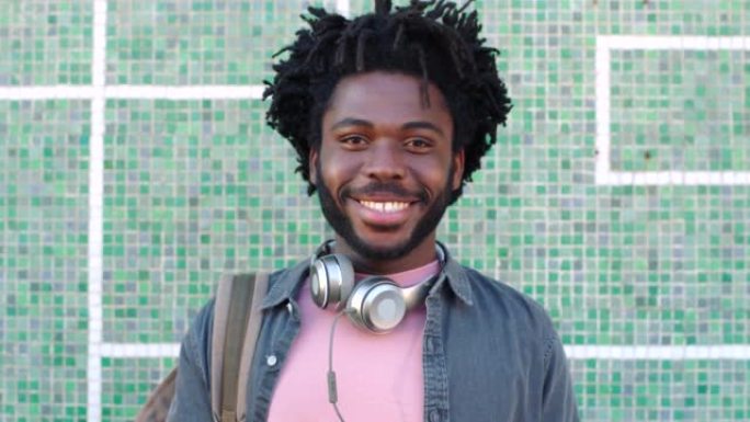 一个年轻的时髦的黑人男学生，辫子站在凉爽的墙外。一个快乐的时尚非洲男人在艺术小镇或城市上音乐学校的肖