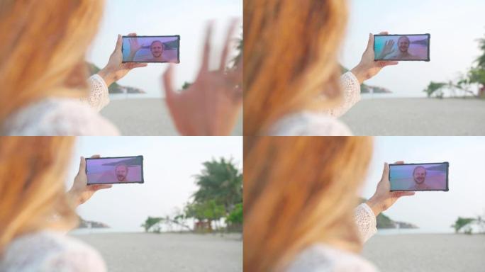 快乐的年轻女子在海滩度假时与男友通过电话进行视频通话时的后视图。现代技术概念的人。