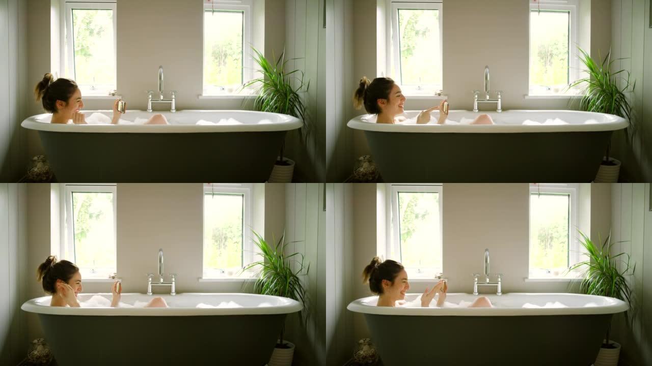 4k视频片段，一名年轻女子在泡泡浴期间在智能手机上进行视频通话