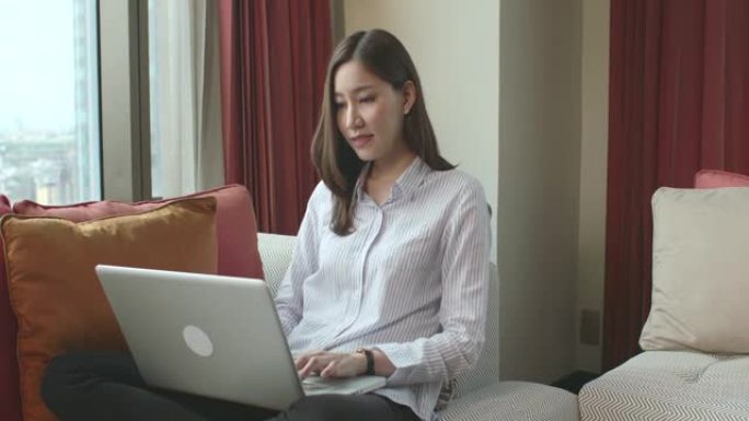 美丽的亚洲女人坐在工作中，膝上放着笔记本电脑。这是对新常态时代的一种适应，因为人们不能外出工作