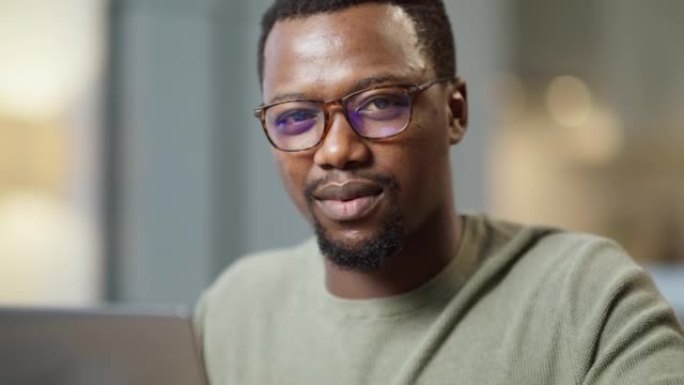 非裔美国商人在家庭办公室使用笔记本电脑的肖像。严肃的黑人企业家独自一人坐在互联网上浏览技术。自信专注