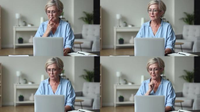 戴着眼镜在笔记本电脑上工作的受启发的老年妇女