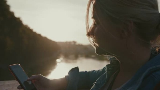 日落时分，SLO MO女人在圣安吉洛桥对面的桥上使用智能手机