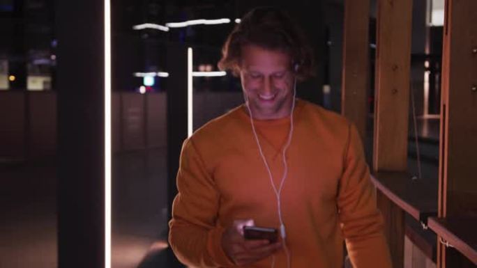 白人男性戴着耳机和滑板，微笑，散步，晚上使用手机