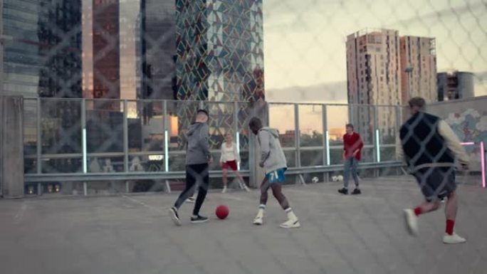 年轻时尚的人在现代城市摩天大楼周围的屋顶上踢足球。年轻的足球运动员盘带，炫耀技巧和躲避对手。篱笆后面