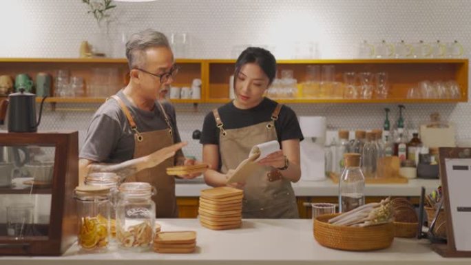 亚洲华人高级男咖啡馆老板在咖啡店柜台安排杯垫时向女儿展示食物菜单