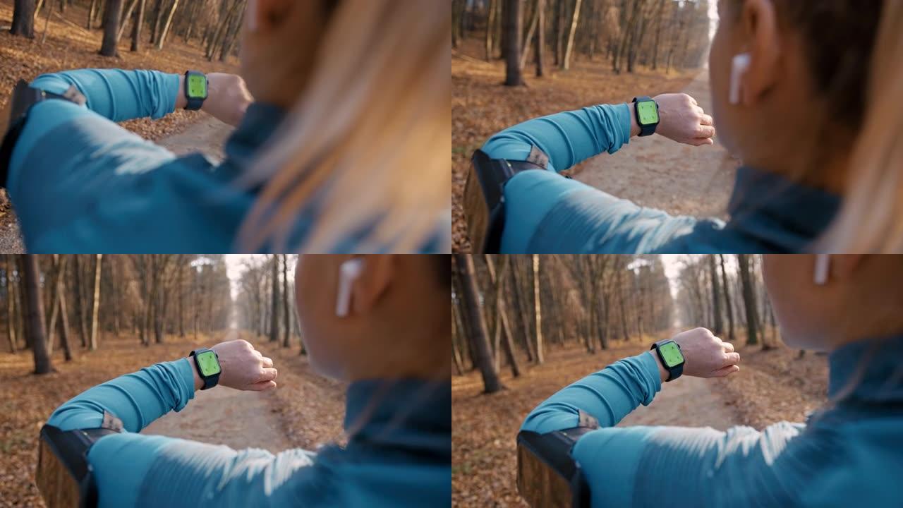 SLO MO女人在穿过森林的道路上停止慢跑后看着她的健身追踪器