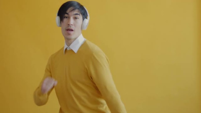 黄色背景上戴着无线耳机跳舞拍手的快乐年轻人肖像