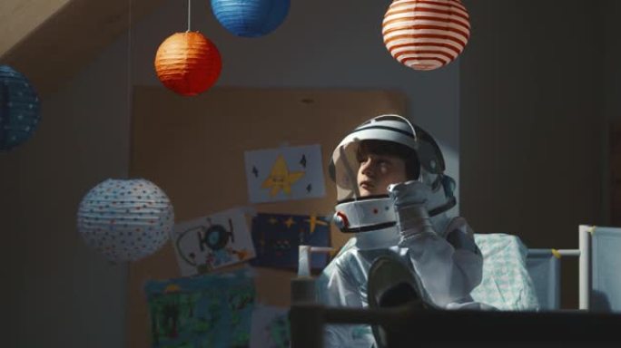 关于太空的梦想。小男孩穿着太空旅行服睡觉，站起来看着阳光，关上头盔遮阳板。