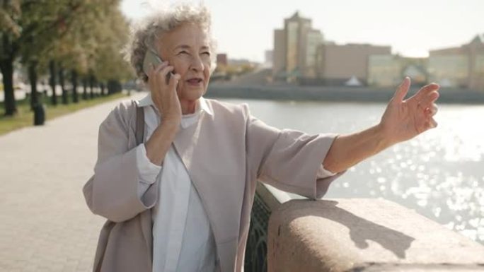 快乐的老太太在大风夏日在河堤外面用手机说话