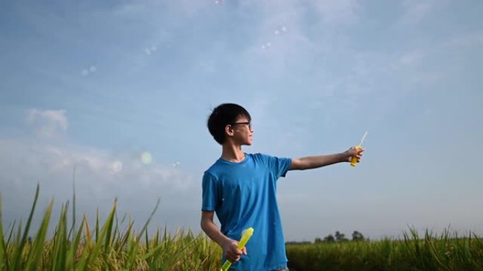 一个亚洲中国男孩在稻田度过了一个有趣的周末，早晨吹泡泡