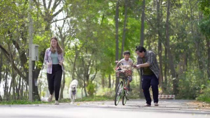 亚洲小男孩喜欢在父母的支持下学习在公园骑自行车。