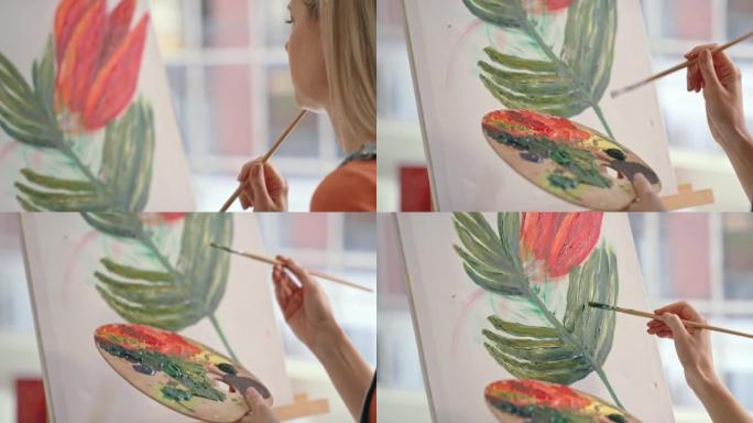 年轻的女画家在工作室里在画布上画彩画。艺术家在车间用画笔画一朵花。女人在僻静的商店里画玫瑰的图像