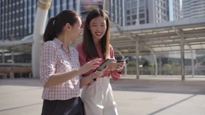 两个亚洲女商人朋友在城市的智能手机上分享了一些东西