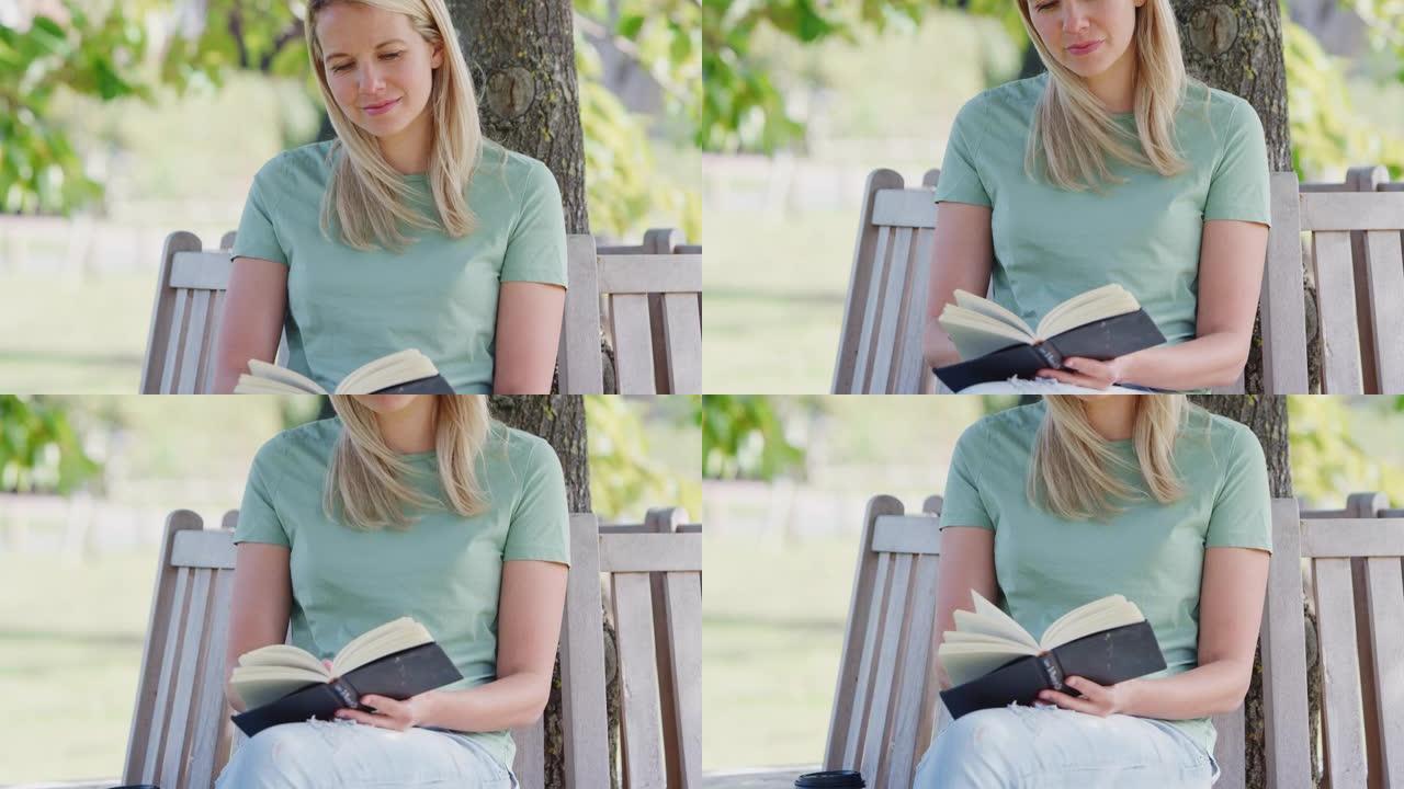 女人坐在树下的公园长椅上读书