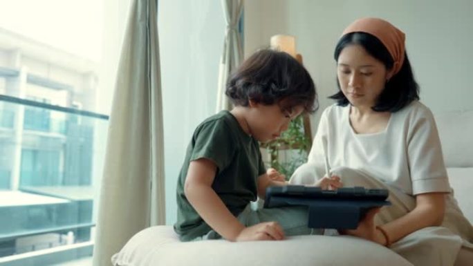 可爱的亚洲妈妈在平板电脑上帮助儿子做作业。