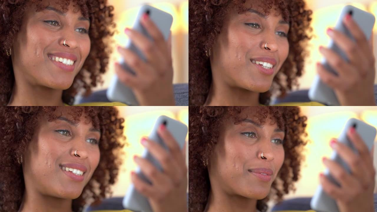 一个女人在视频通话中的脸，独自坐在沙发上聊天，看起来很开心。快乐的非洲女性，卷发微笑着与朋友或家人聊