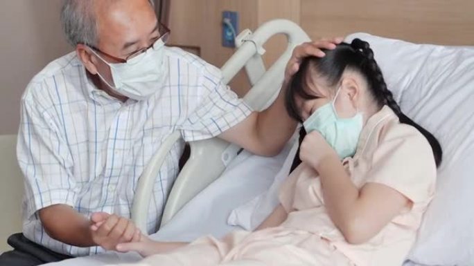 在医院里，快乐的亚洲祖父或56岁的父亲拜访了她康复中的9岁的孙女，她躺在床上，牵着手安慰。祖父母和孙