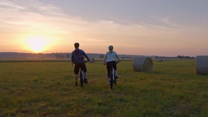 SLO MO几个骑自行车的人停下来欣赏草地上的日落