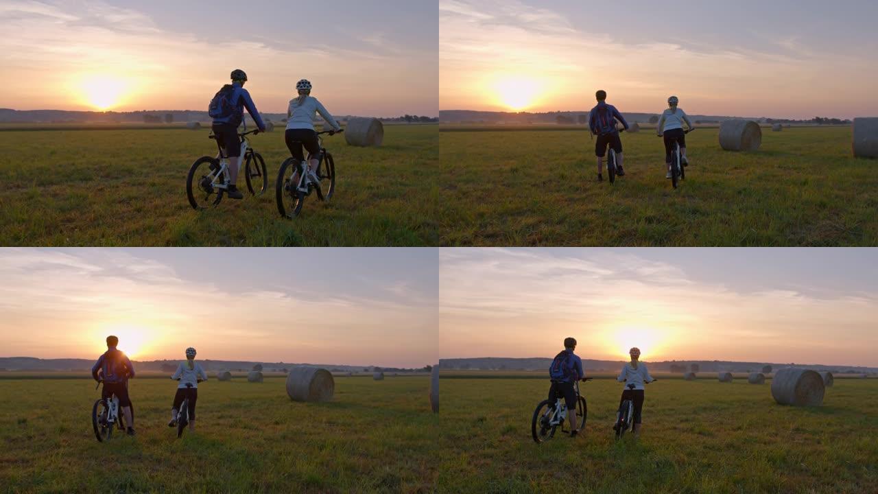 SLO MO几个骑自行车的人停下来欣赏草地上的日落