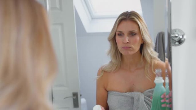 成熟的女人在家里的浴室里用漱口水照镜子