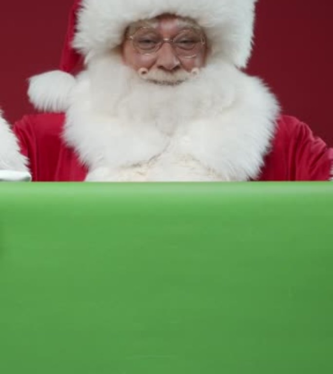 一个微笑的圣诞老人在红色背景上进入绿色屏幕后面的框架的垂直视频