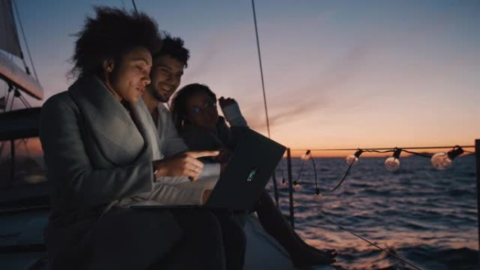 SLO MO一群朋友在黄昏航行的帆船上使用笔记本电脑