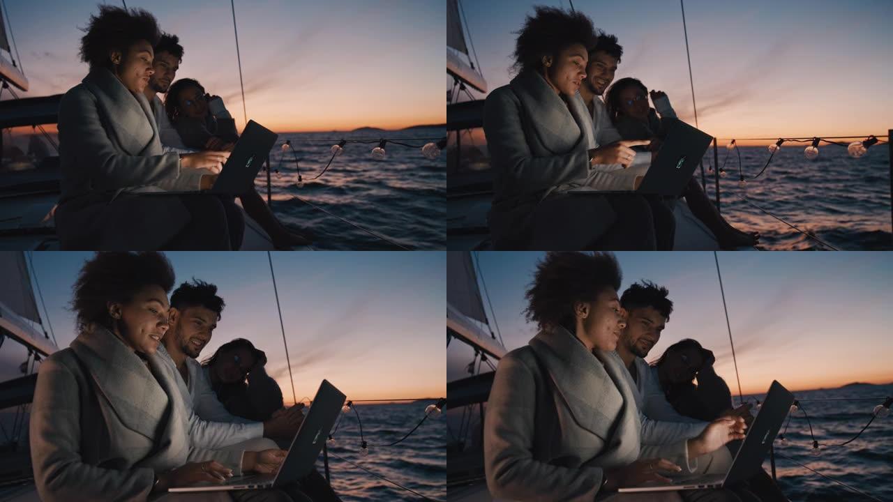 SLO MO一群朋友在黄昏航行的帆船上使用笔记本电脑