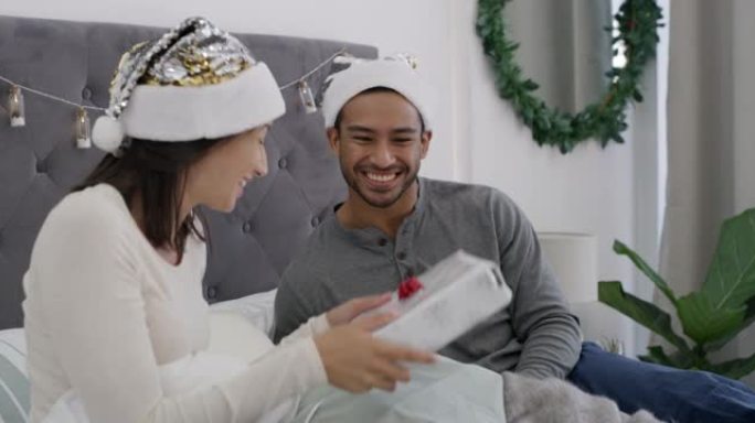 4k视频片段，一对年轻夫妇在圣诞节早上一起在家里的床上交换礼物