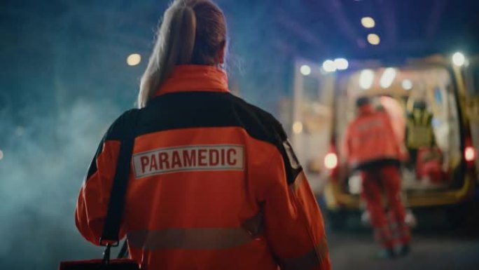 女性EMS护理人员自豪地站着，背对着镜头，穿着带有 “护理人员” 文字标志的高可见度医用橙色制服。成
